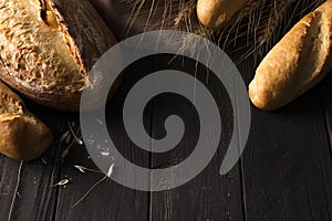 Bakery - gold rustic crusty loaves of bread and buns on black background.