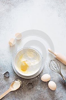 Bakery ingredients-wheat flour, raw eggs and kitchen utensils on a gray stone backgound