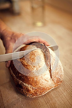 Bakery man, chef cut on wooden cutting board just prepared, delicious, hot loaf of bread with golden brown crispy crust