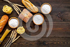 Bakery production, making bread and pasta. Fresh bread and raw pasta near flour in bowl and wheat ears on dark wooden