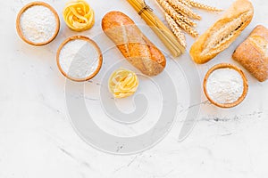 Bakery production, making bread and pasta. Fresh bread and raw pasta near flour in bowl and wheat ears on white stone