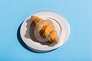 Bakery products baked croissant on white plate. Blue background, top view close-up. Pop art style. Summer shadows