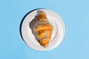 Bakery products baked croissant on white plate. Blue background, top view close-up. Pop art style. Summer shadows