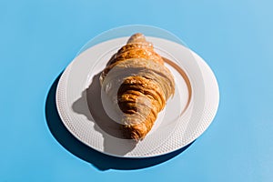 Bakery products baked croissant on white plate. Blue background, top view close-up. Pop art style. Summer shadows