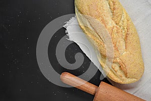 Bakery - rustic crusty loaves of bread and rolling pin on linen cloth over black chalkboard background.