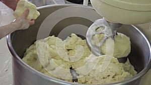 The bakery worker hands helps stir the dough in the kneader.