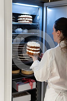 Bakery worker inserts Red Velvet cake into a fridge full of cupcakes, cakes and desserts. one with a gift bow