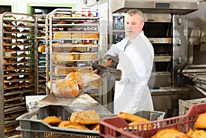Bakery worker pulling loaves from oven