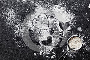 Baking background with flour and heart shape on kitchen black table from above for Valentines day cooking. Flat lay style.