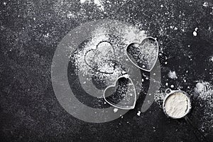 Baking background with flour and heart shape on kitchen black table top view for Valentines day cooking. Flat lay.