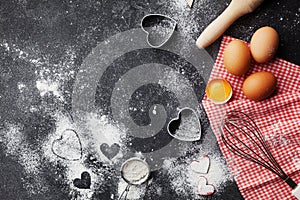 Baking background with flour, rolling pin, eggs, and heart shape on dark kitchen table top view for Valentines day cooking. Flat l