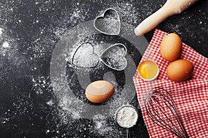 Baking background with flour, rolling pin, eggs, and heart shape on kitchen black table top view for Valentines day cooking.