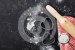 Baking background with flour, rolling pin and heart shape on kitchen black table top view for Valentines day cooking. Flat lay.