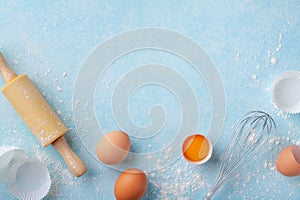 Baking background with rolling pin, whisk, eggs, flour on blue table top view. Flat lay