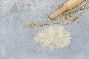 Baking background with whole grain flour, wheat ears and rolling pin on grey concrete background. Top view, copy space