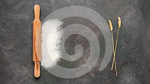 Baking background. Wooden rolling pin, flour and ears of wheat on a dark grunge background. Top view, flat lay. Banner.