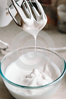 Baking concept. Whipped cream of egg whites for perfect peaks in a glass bowl, with a mixer on a marble white table. Meringue