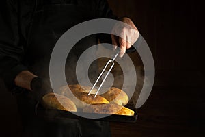 Baking delicious pies for the festive table. A baking sheet in baker's hand with freshly baked buns and a fork. Space for