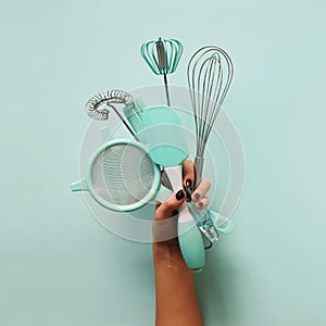 Baking flat lay. Female hands holding kitchen tools, sieve, rolling pin, spatula and bruch on pastel blue background. Banner with