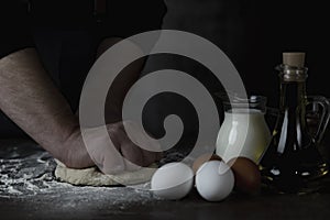 Baking fresh bread in the bakery, hands of male knead dough on kitchen table with flour