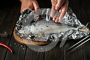 Before baking, fresh fish must be wrapped in foil and aromatic spices and peppers must be added. Close-up of chef hands while