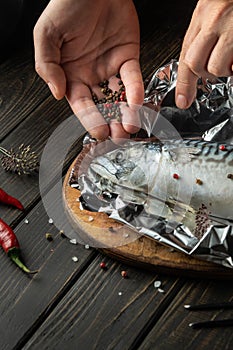 Before baking, fresh fish must be wrapped in foil and aromatic spices and peppers must be added. Close-up of chef hands while