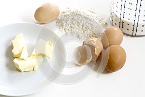 Baking ingredients, butter, eggs, flour and milk on a white back