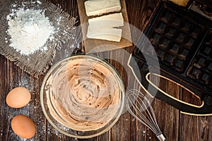 Baking ingredients for cooking chocolate waffles or cake. Bowl with sugar, eggs, flour, butter on dark wooden background.