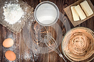 Baking ingredients for cooking chocolate waffles or cake. Bowl with sugar, eggs, flour, butter on dark wooden background.