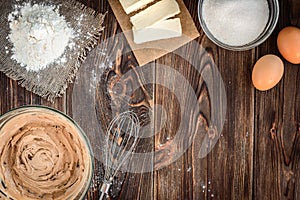 Baking ingredients for cooking chocolate waffles or cake. Bowl with sugar, eggs, flour, butter on dark wooden background.