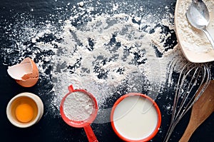 Baking ingredients on a dark, stone table: eggs, flour and milk