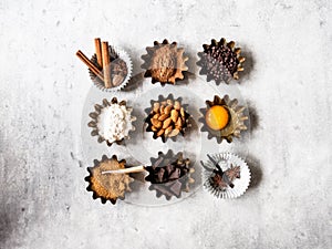 Baking ingredients: flour, brown sugar, egg, cocoa, almond, dark chocolate and spices on a grey background. Top view