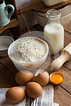 Baking ingredients flour, eggs, open yolk, milk, rolling pin, cupboard, rustic interior