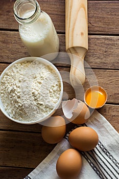 Baking ingredients flour, eggs, open yolk, milk, rolling pin, linen towel, rustic kitchen interior, utensils