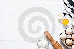 Baking ingredients: flour, eggs, sugar with a rolling pin on a light white wood background. With copy space