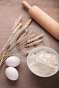 Baking ingredients. Flour, eggs, wheat and rolling pin on table cloth.