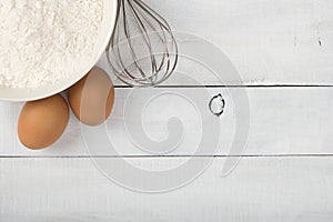 Baking Ingredients of White Flour and Farm Fresh Brown Eggs with a Whisk on Distressed Shiplap Wood Board Table with room or spac