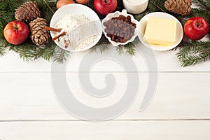 Baking ingredients on white table. eggs, butter, spice, apples, raisins, vanilla and cinnamon sticks, white flour and xmas tree