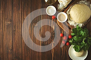 Baking in rural kitchen. Dough and ingredients for baking pizza on vintage brown wooden table. Top view. Rustic background
