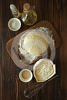 Baking in rural kitchen. Dough and recipe ingredients on vintage brown wooden table. Top view. Rustic background