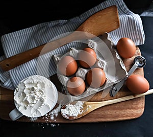 Baking setup including 6 eggs a cup of flower, spatula, wooden spoon