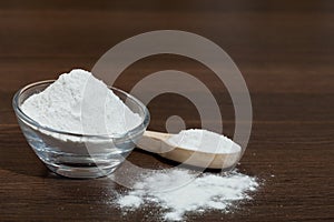 Baking soda - glass bowl and wooden spoon with baking soda; on dark wooden background
