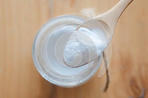 Baking soda in glass bowl and wooden spoon on wooden background