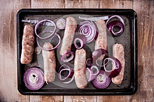 Baking tray with six raw pork and apple sausages