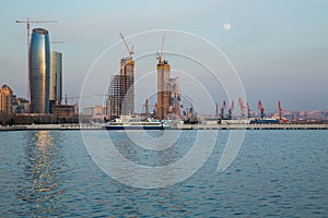 Baky skyline view from Baku boulevard the Caspian Sea embankment . Tall buildings in Baku. Ship cranes . Moon. harbor . Port