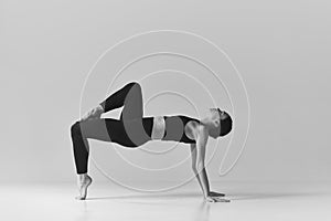 Balance. Black and white photography. Young slim, fit girl training, doing stretching exercises over studio background