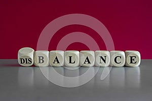 Balance or disbalance symbol. Turned a cube and changes the word disbalance to balance. Beautiful red background, grey table, copy