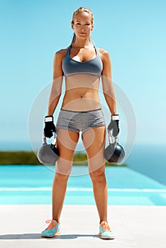 Balance is...a kettle bell in each hand. Full length portrait of a beautiful young woman exercising with kettle bells