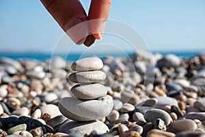 Balance of mind - abstract - hand putting pebble on the tower of stones on the sunny beach