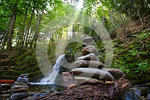 Balance pyramid of stones on the shore of a forest waterfall on a sunny morning